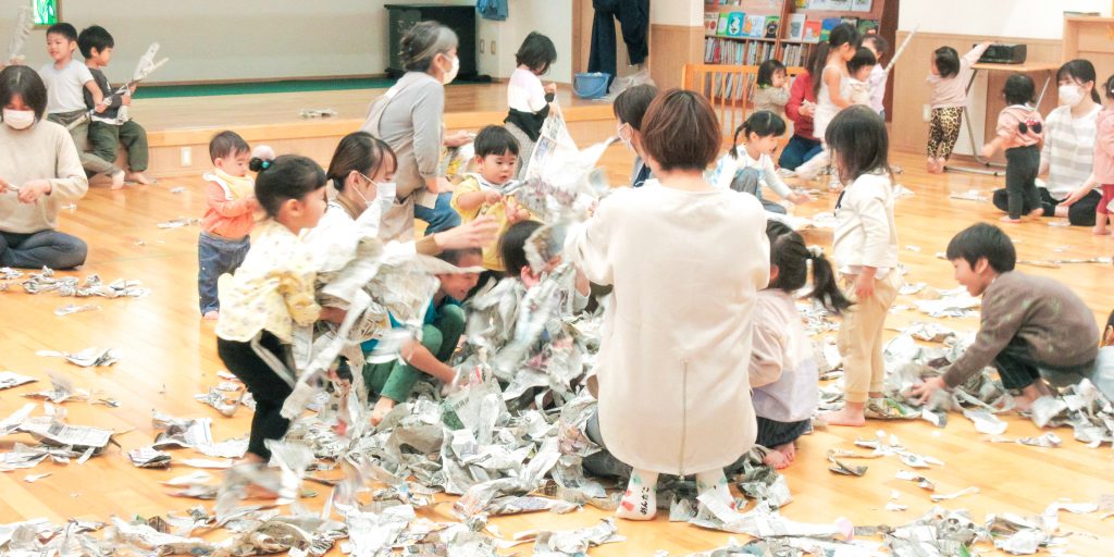誕生会で新聞紙をくしゃくしゃにして遊ぶ園児たち