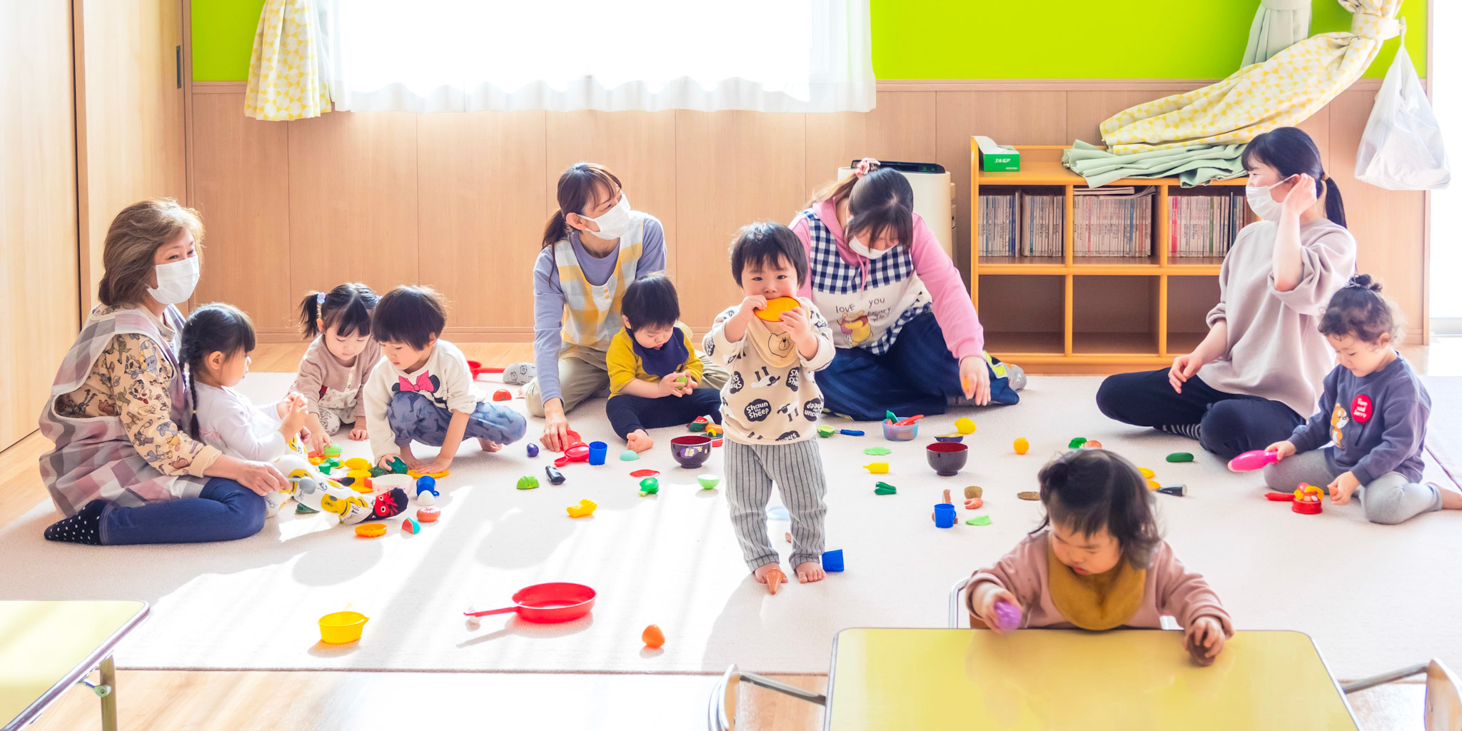保育室で遊ぶ3才未満の園児たちと保育士たち