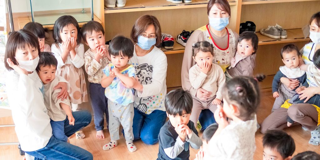 避難訓練中に玄関で待機する保育士と園児