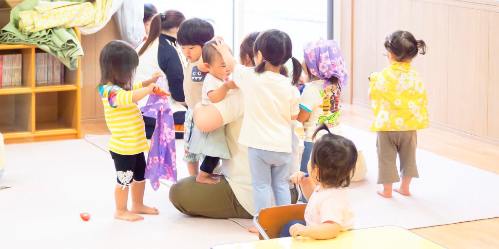 3才児未満の園児たちに囲まれる保育士