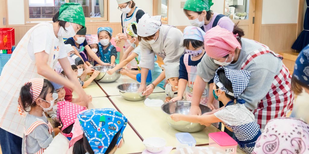 クッキング保育で調理する保育士とサポートする園児たち
